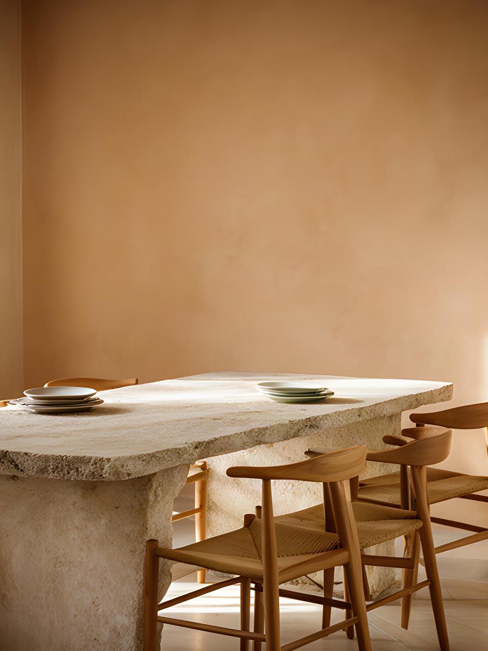 Dettaglio di una zona pranzo campana con tavolo in pietra, sedie in legno e parete color sabbia